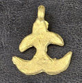 Small brass Akokɔnan pendant with curved projecting arms, two open side cutouts, and a top hanging loop on dark textured fabric