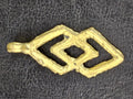 Brass Epa pendant with two linked angular openwork sections and a hanging loop on the left, lying on dark textured fabric