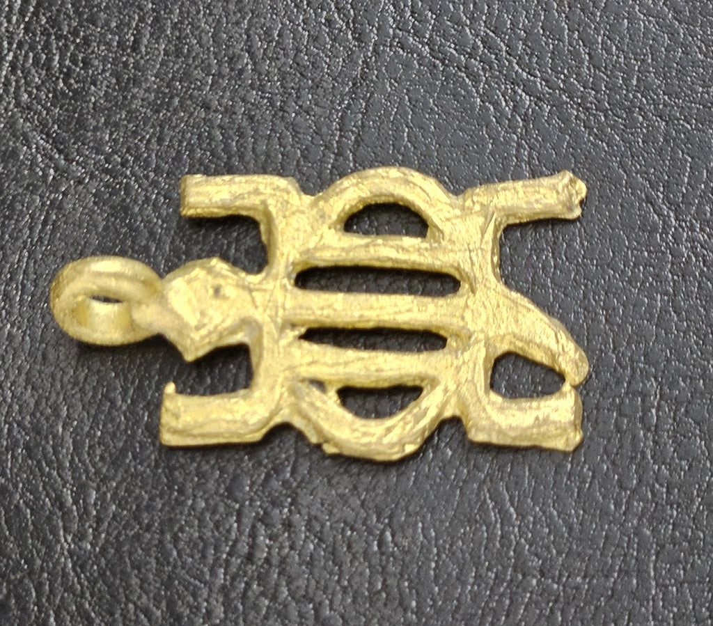 Brass openwork pendant lying horizontally, with its hanging loop on the left, on a dark textured background.