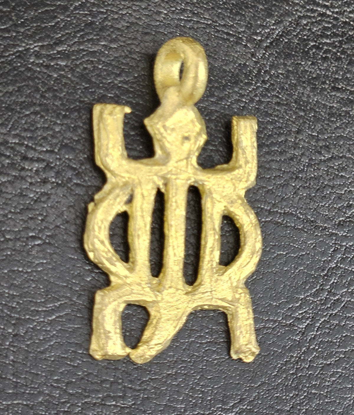 Brass openwork pendant with an oval center, projecting corners, and a top hanging loop on a dark textured background.