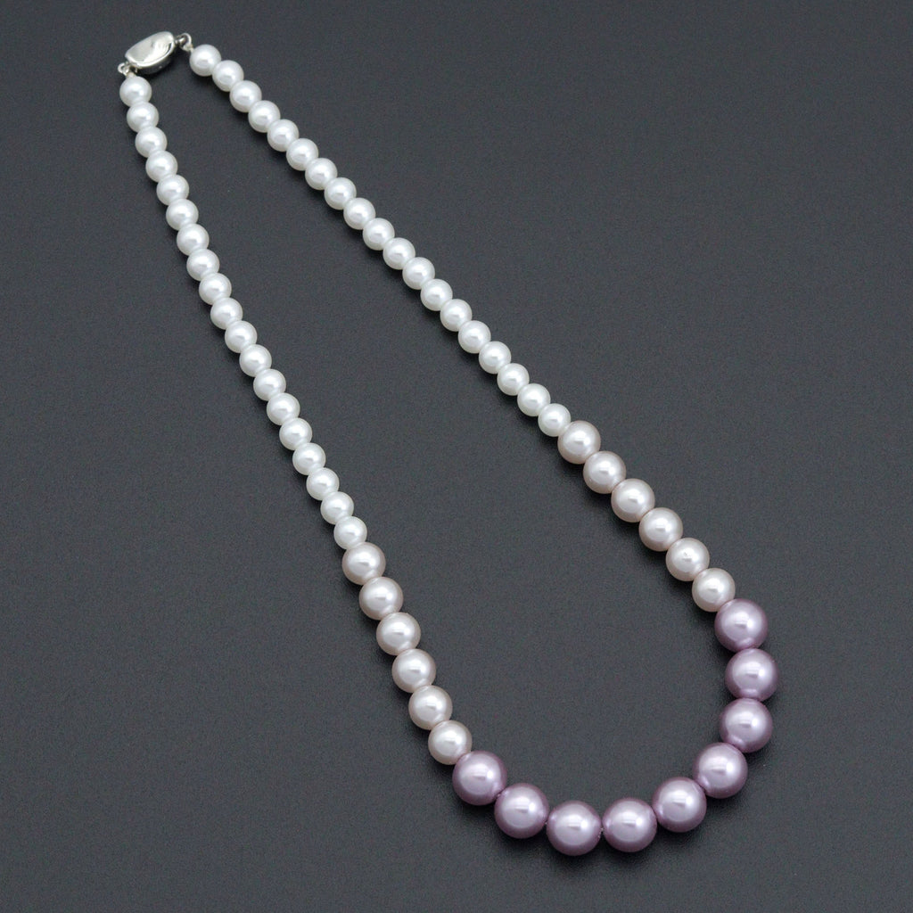 Purple gradient pearl bead necklace laid on a dark background