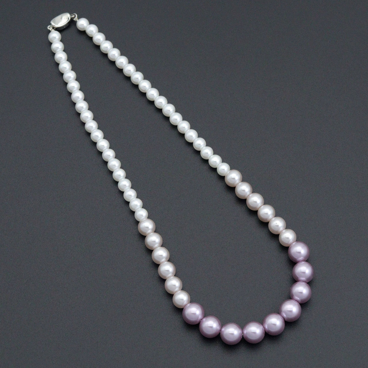 Purple gradient pearl bead necklace laid on a dark background