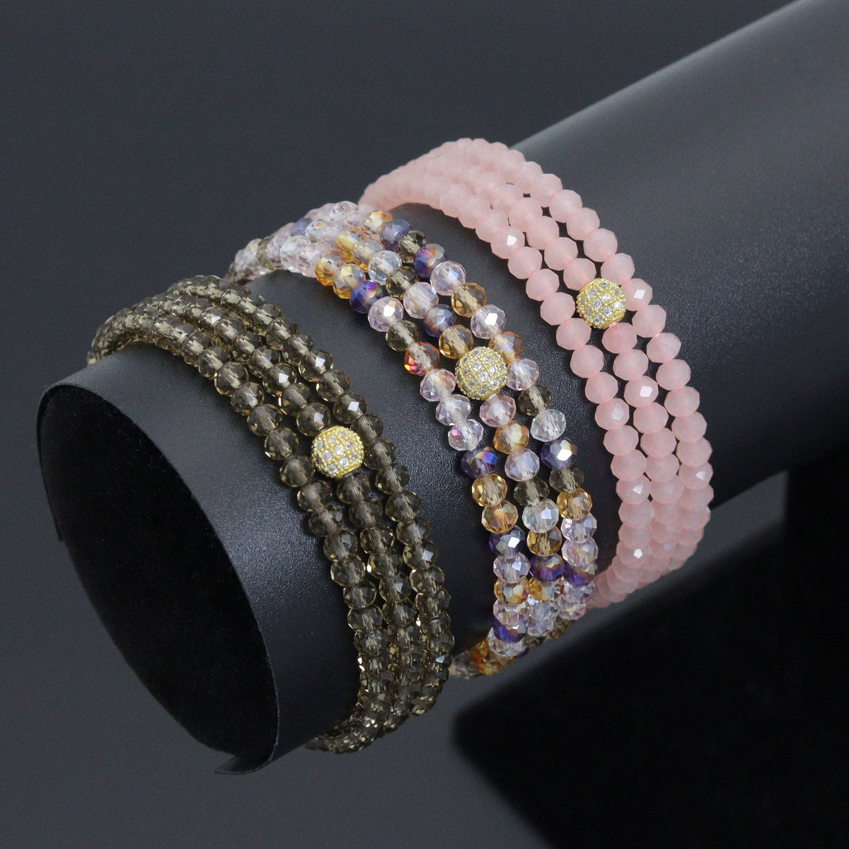 Smoky brown, multicolored and pale pink crystal wrap bracelets on a black display stand