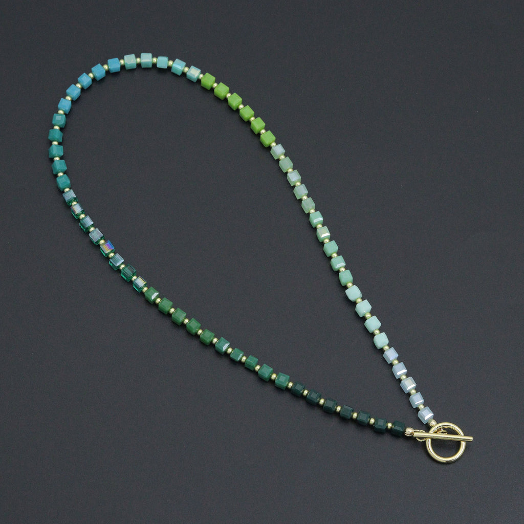 Ombré green cube bead necklace with gold-tone spacers and a toggle clasp on a dark background