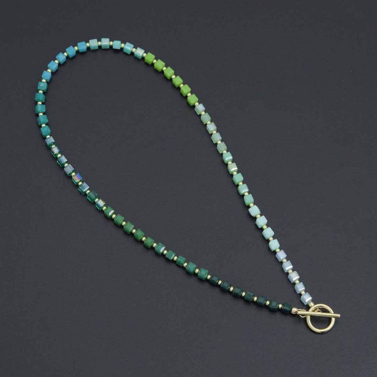 Ombré green cube bead necklace with gold-tone spacers and a toggle clasp on a dark background