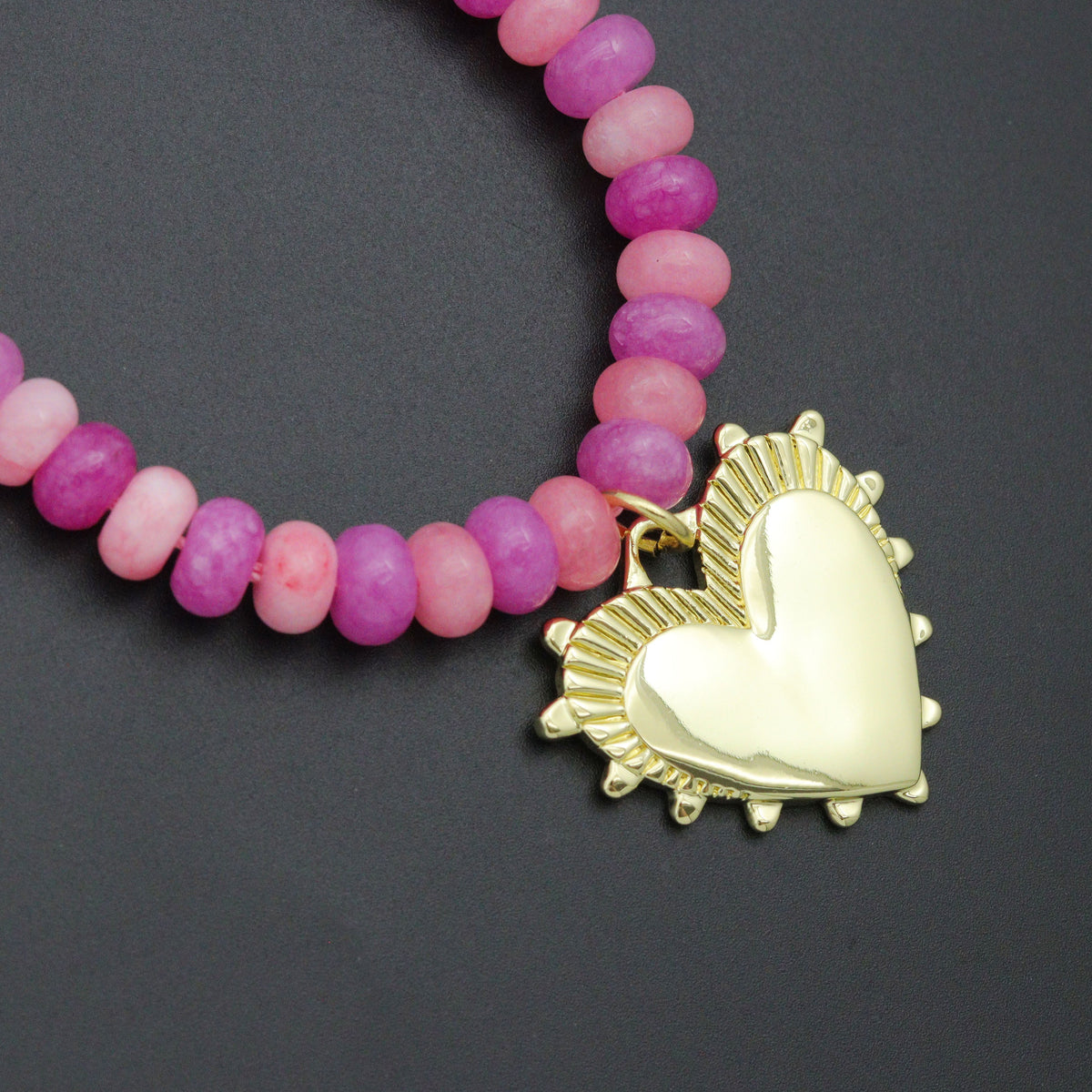 Close-up of alternating pink and magenta beads and a textured gold-tone heart pendant