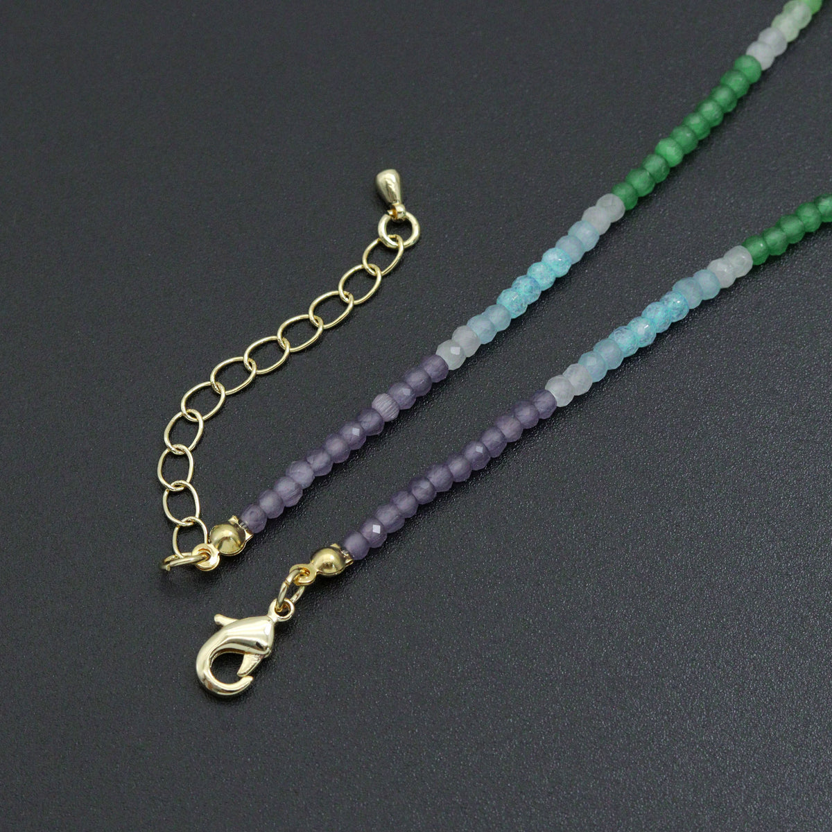 Rainbow bead necklace gold-tone lobster clasp and extender beside purple, blue and green beads