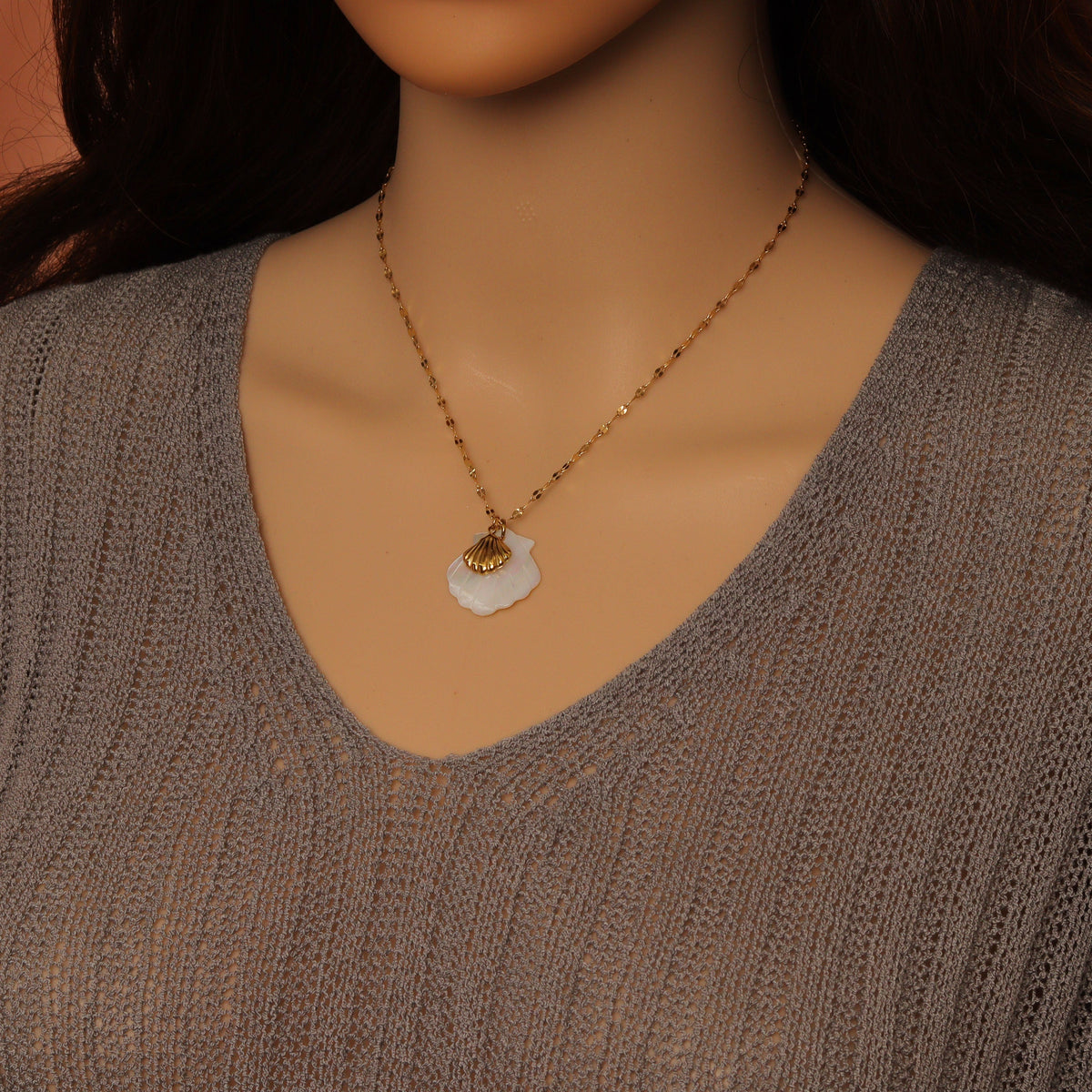 White shell pendant and small gold-tone shell charm necklace worn over a gray top