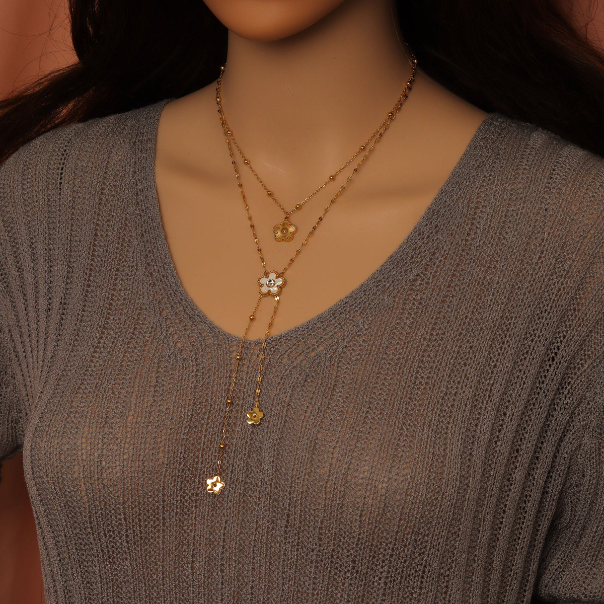 Layered gold-tone flower necklace worn with dangling charms over a gray top