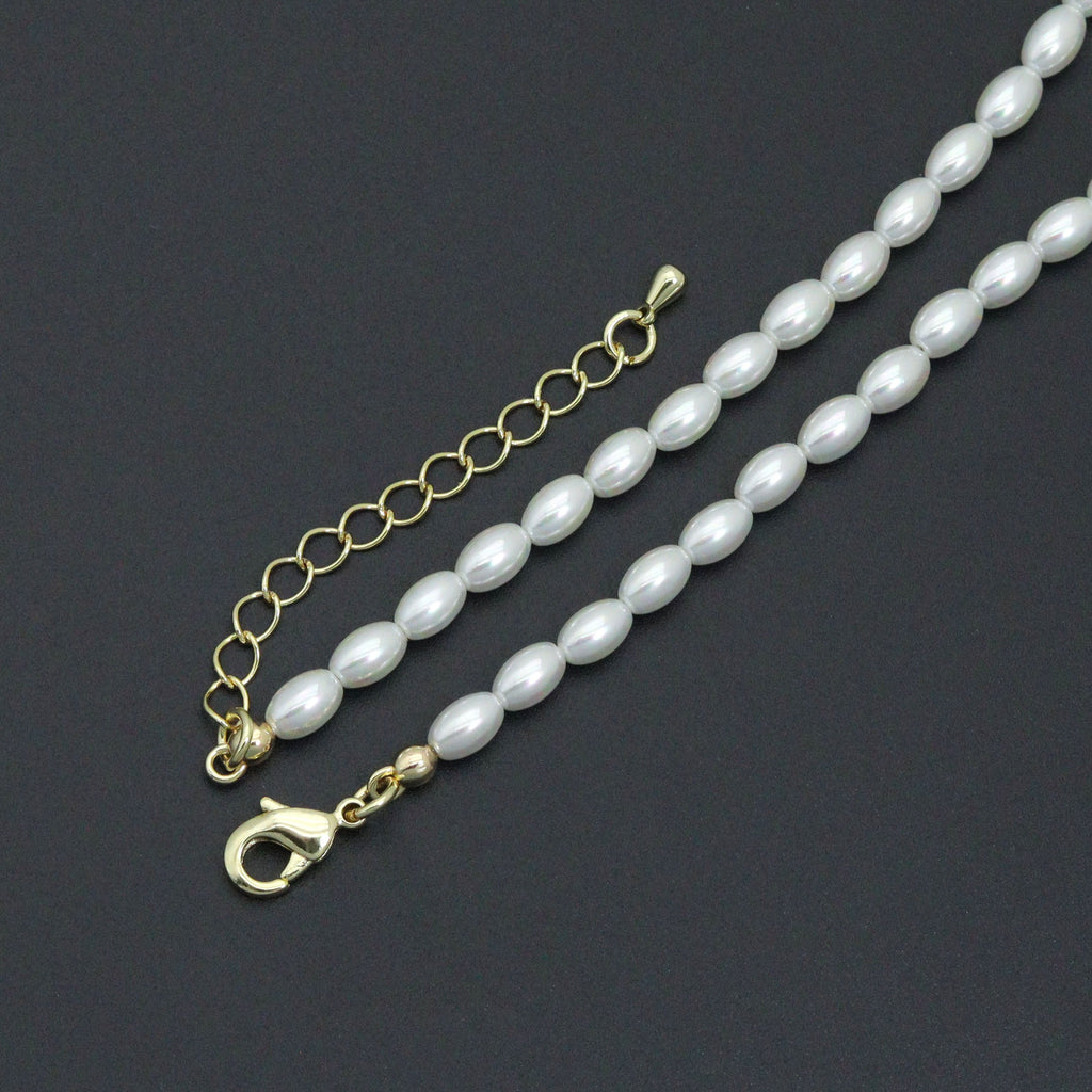 Close-up of white rice-shaped beads, a gold-tone lobster clasp and extender chain