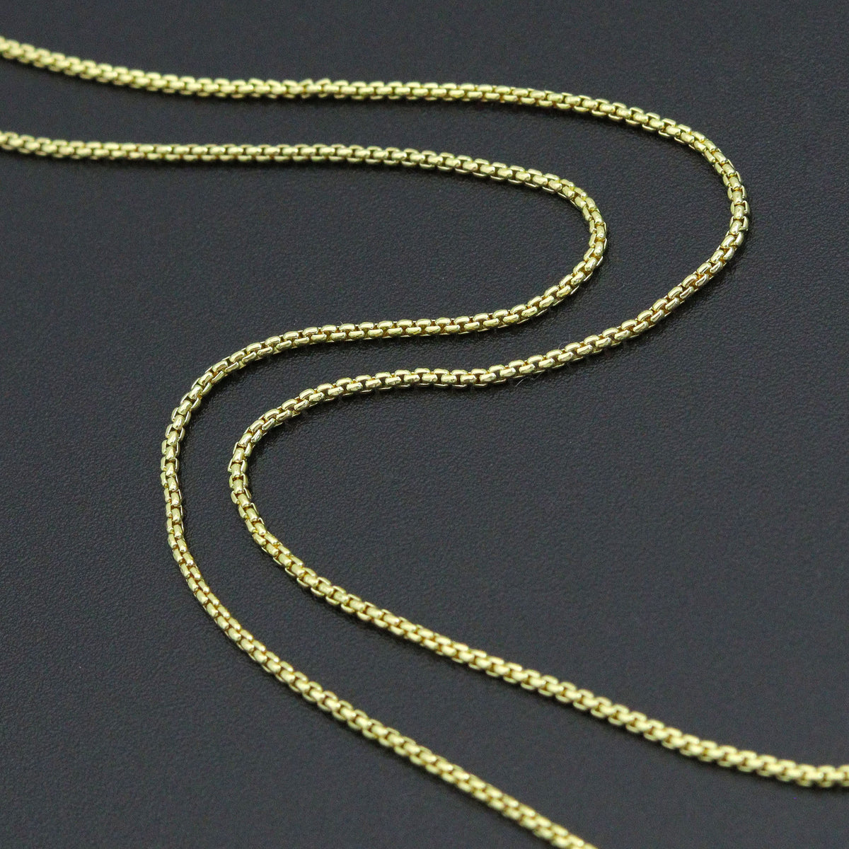 Close-up of the gold-tone thin box chain links on a dark background