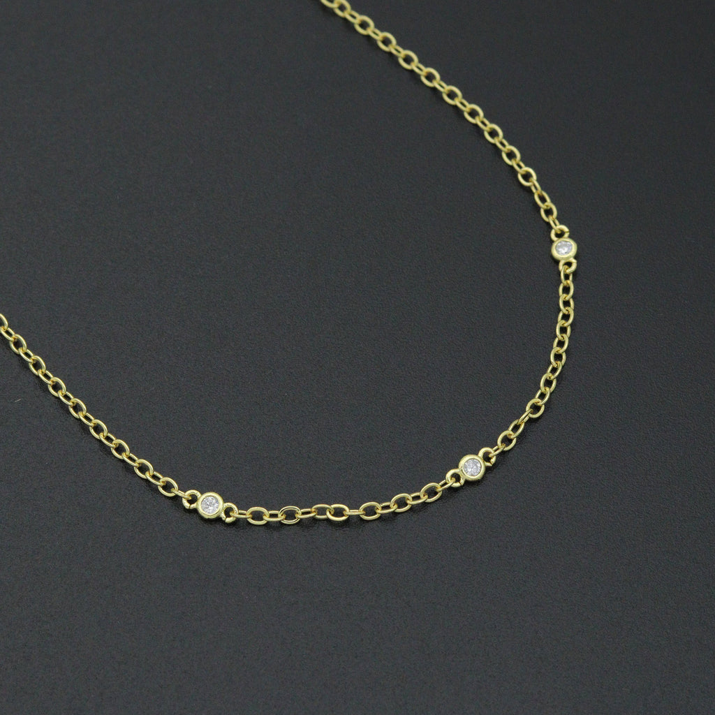 Close-up of clear stones in round gold-tone bezels spaced along a fine link chain