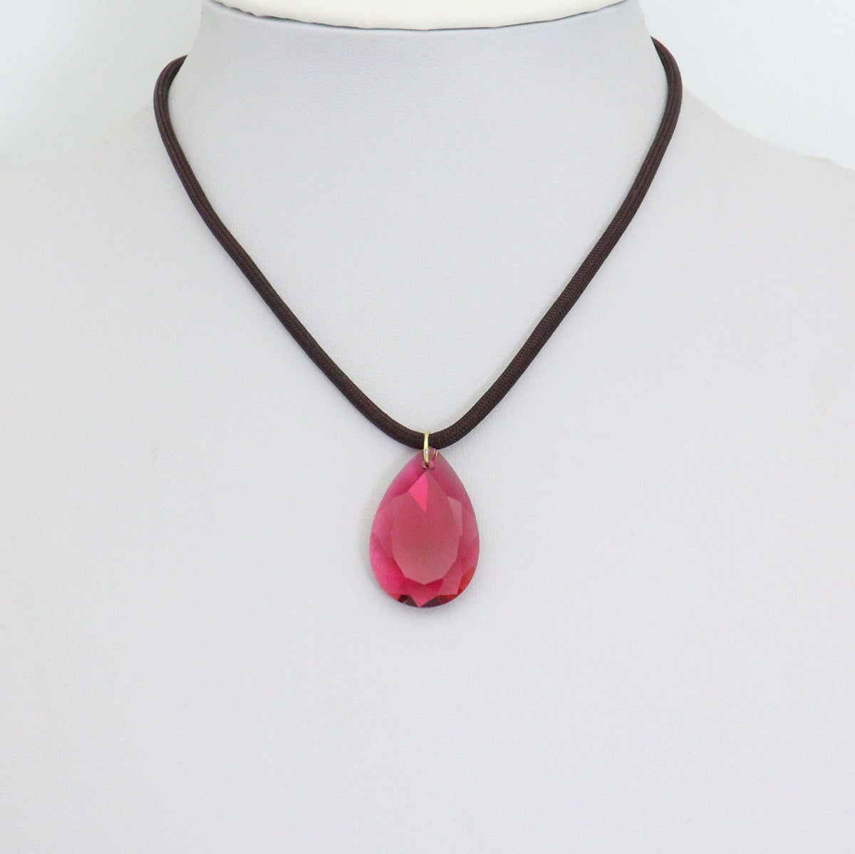 Dark cord necklace displaying a pink teardrop pendant on a white bust