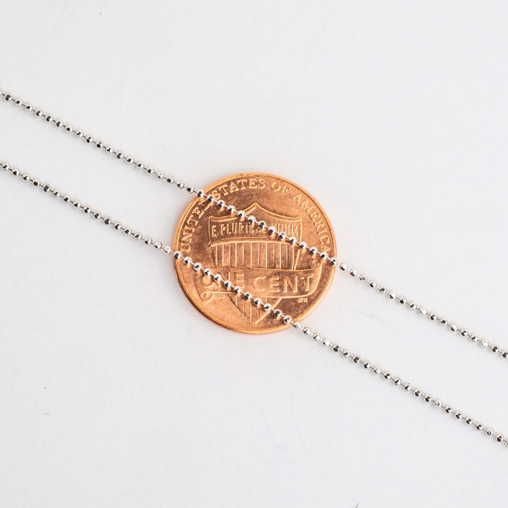 Close-up of small silver ball chain beads over a penny for scale