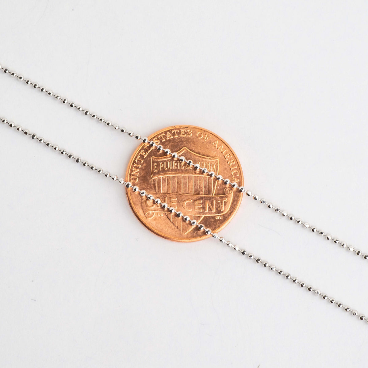 Close-up of small silver ball chain beads over a penny for scale