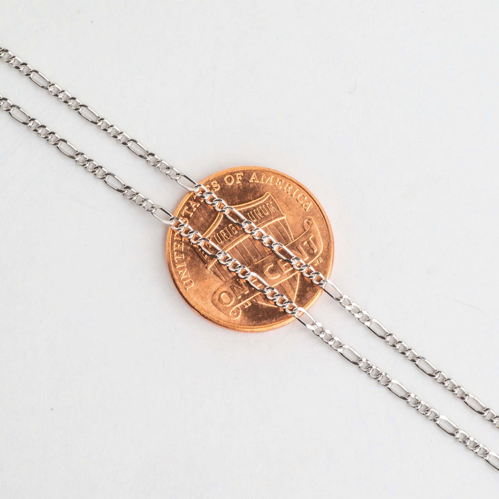 Close-up of alternating long and short Figaro chain links over a penny