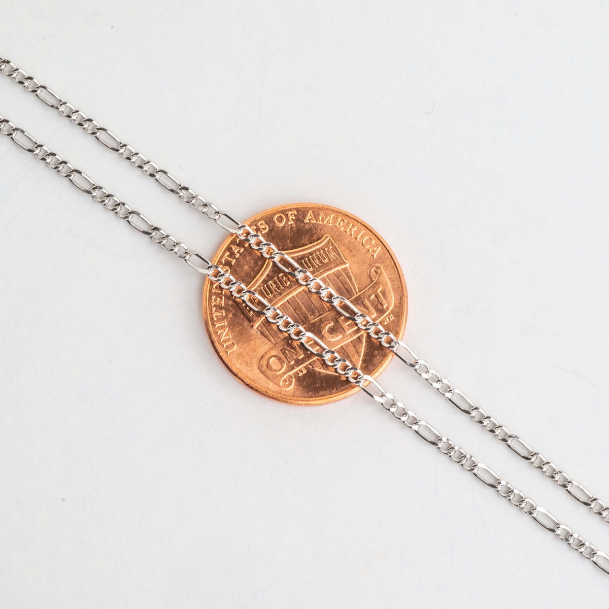 Close-up of alternating long and short Figaro chain links over a penny