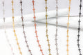 Specialty chains with repeating cross-shaped links in multiple finishes over white display props.