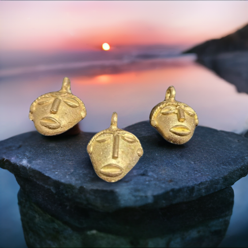 3 african brass small tribal mask pendants sunset background close up