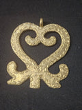 Brass Sankofa pendant in an open heart-shaped design with inward curls, textured surface patterns, and a top hanging loop on dark fabric