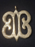 Brass Hye Won Hye pendant with four curled open loops around an elongated central opening, grooved surface details, and a top hanging loop on dark fabric