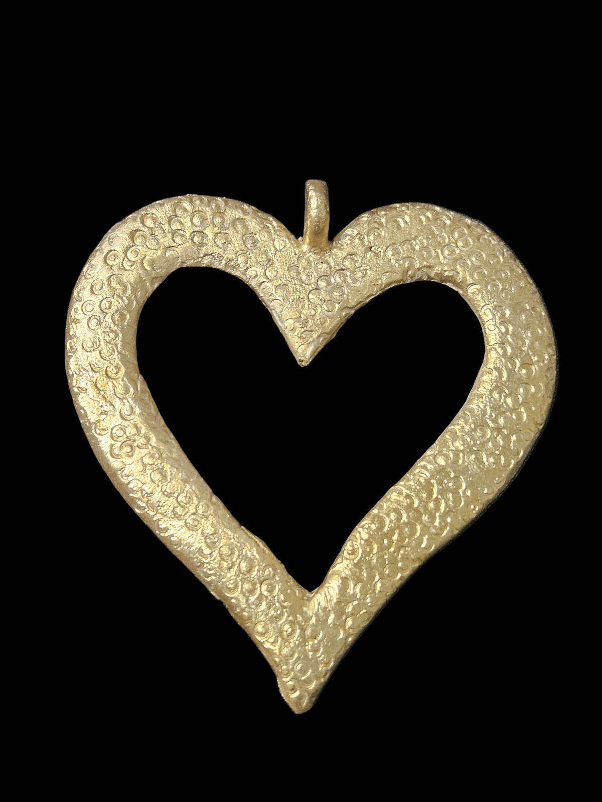 Brass Akoma pendant in an open heart shape with small circular surface patterns and a top hanging loop against a black background