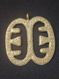 Brass Ese Ne Tekrema pendant with two elongated open sections, inward-facing bar details, a patterned surface, and a top hanging loop on dark fabric.