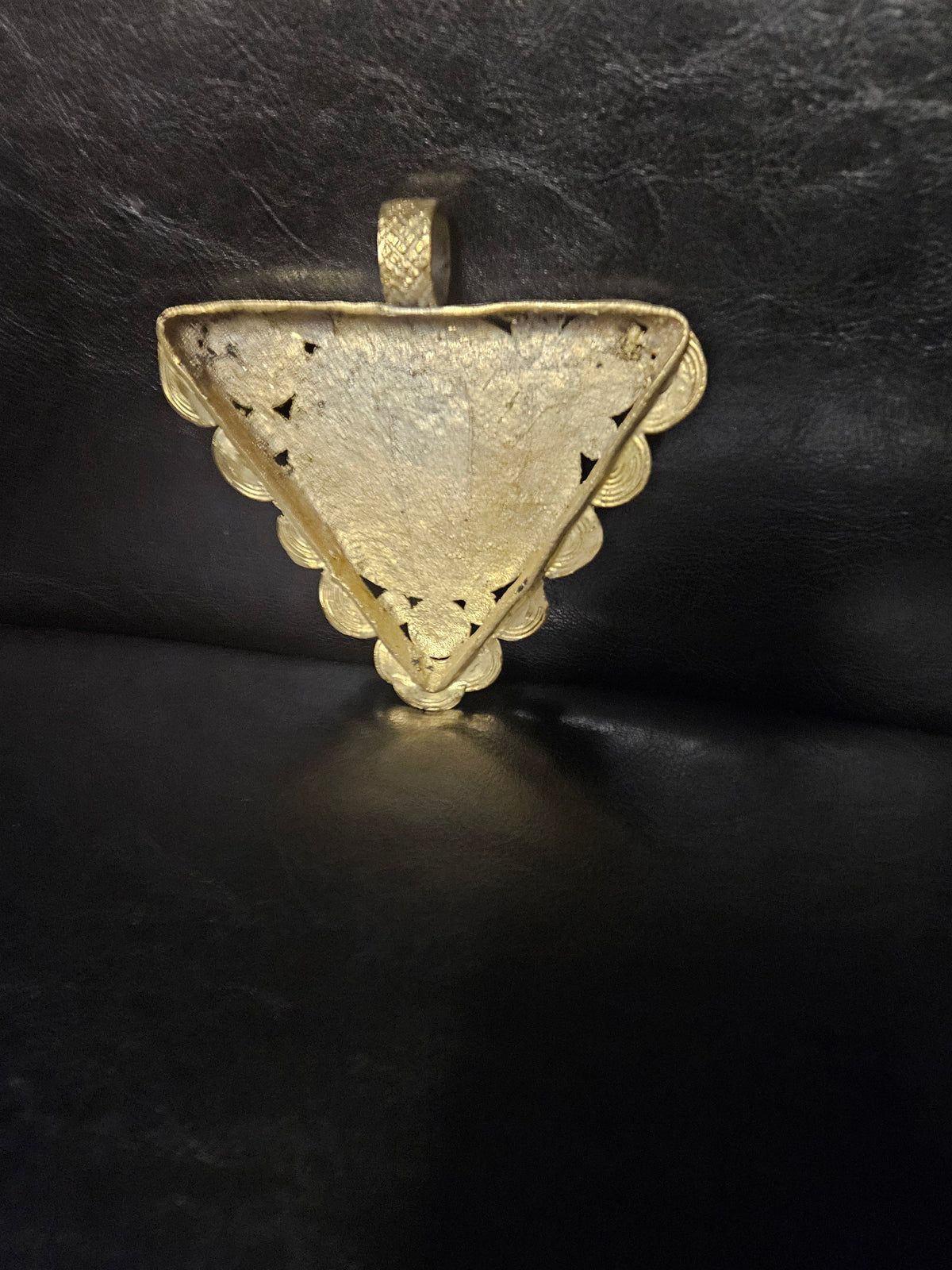 Rear view of the triangular brass Akofena pendant showing its central back panel, spiral border, and top hanging loop
