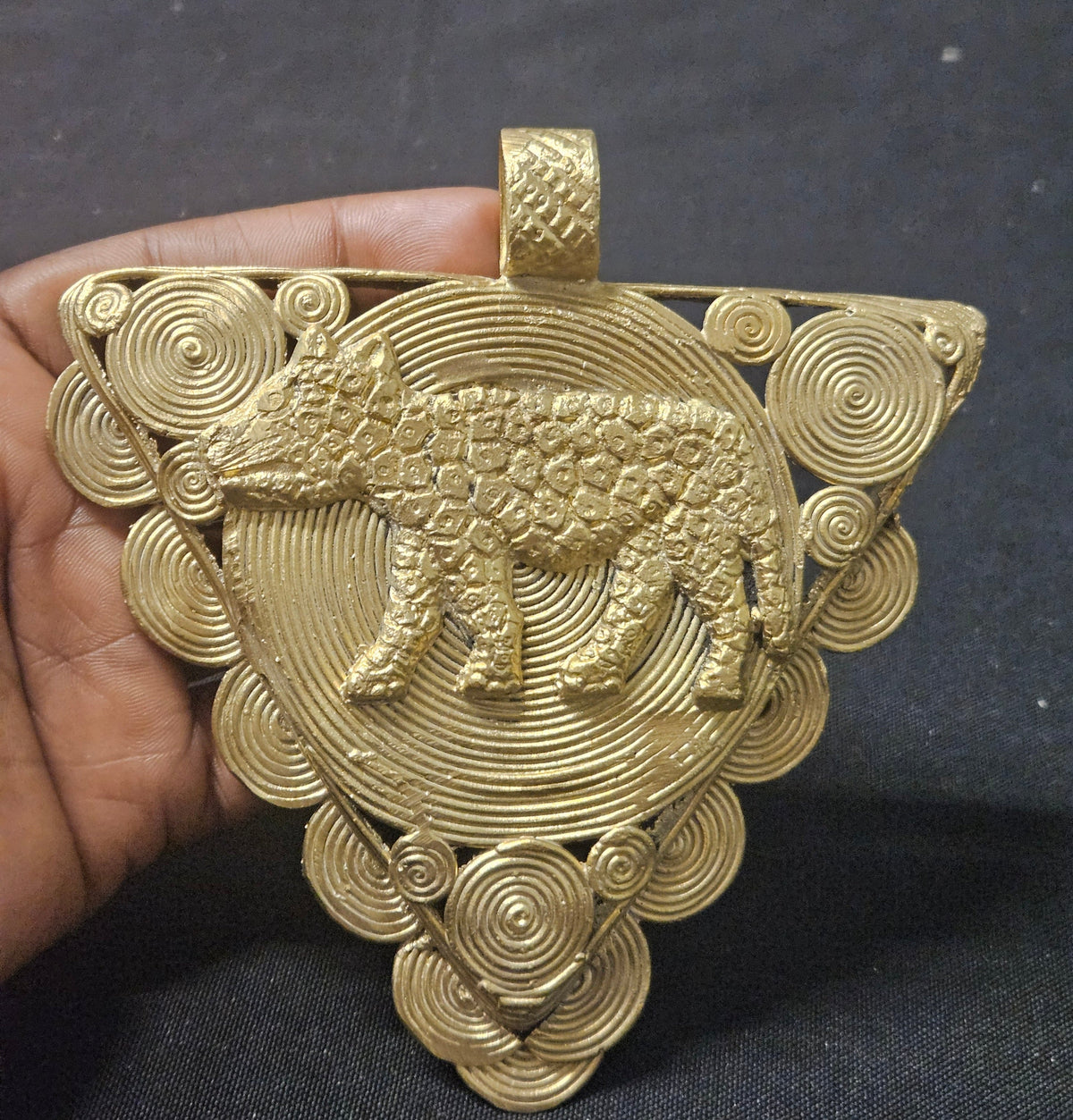 Triangular brass leopard pendant held in a hand, showing the front spiral disc design and top hanging loop