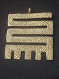 Brass Nkyinkyim pendant with a zigzag openwork design, textured surface patterns, short prongs along the bottom, and a top hanging loop on dark fabric