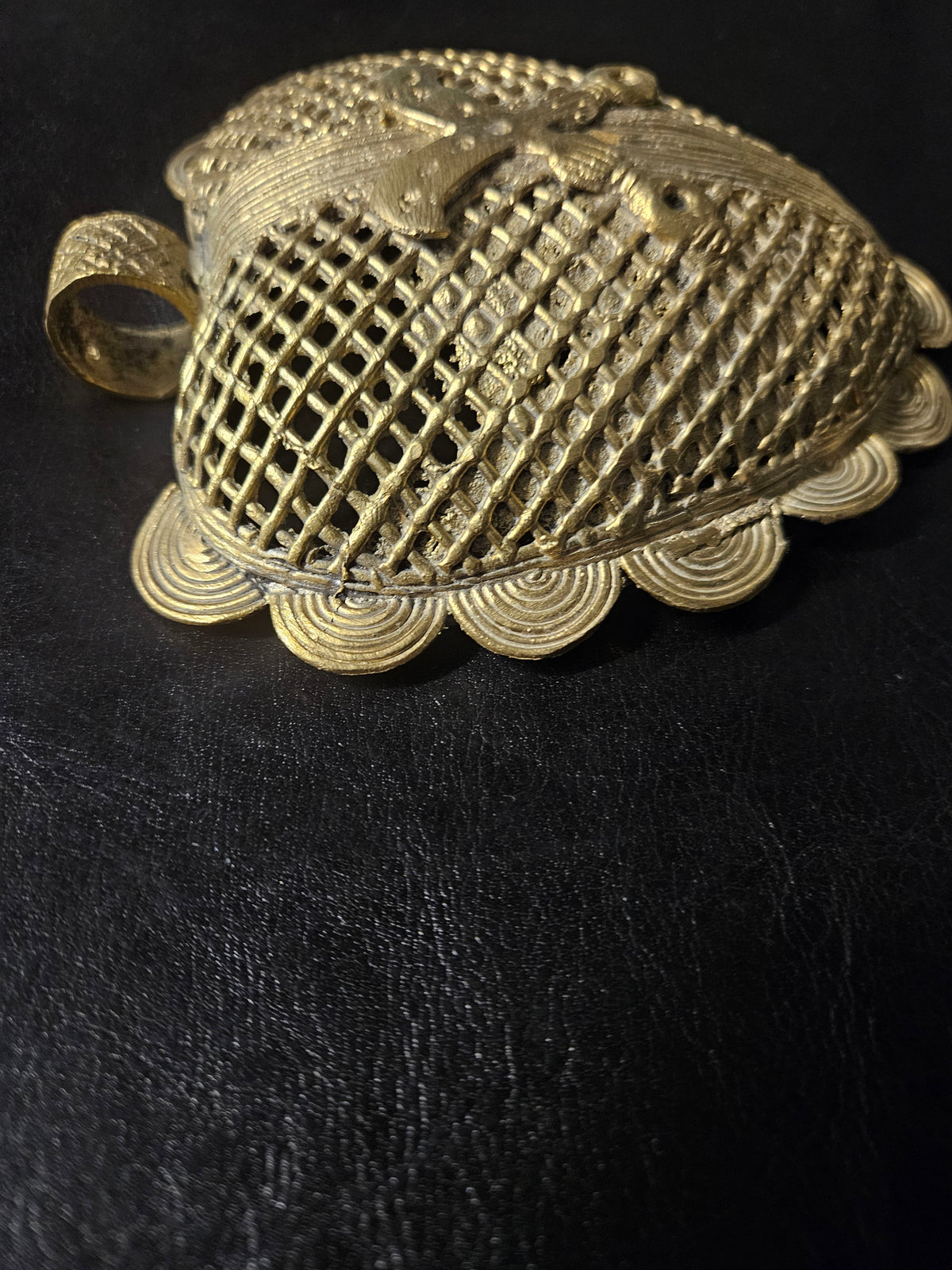 Angled view of the brass Sankofa bird pendant showing its raised bird motif, open diamond lattice, spiral edging, and hanging loop