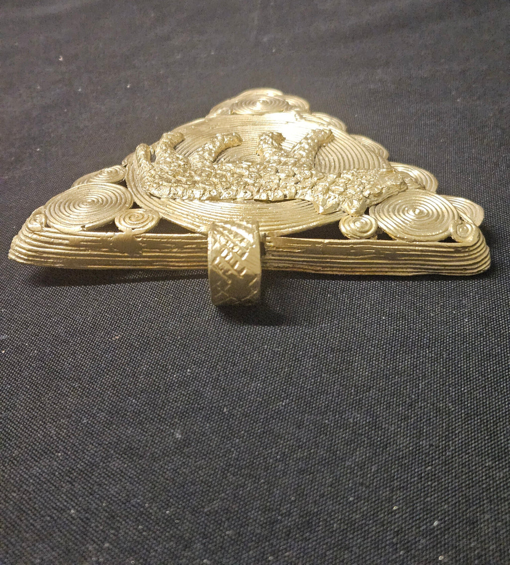 Low side view of the triangular brass leopard pendant showing its thickness, raised detailing, and hanging loop