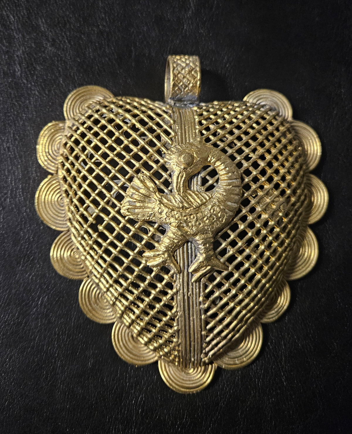 Brass pendant with a raised backward-looking Sankofa bird over a diamond lattice background, scalloped spiral borders, and a top hanging loop