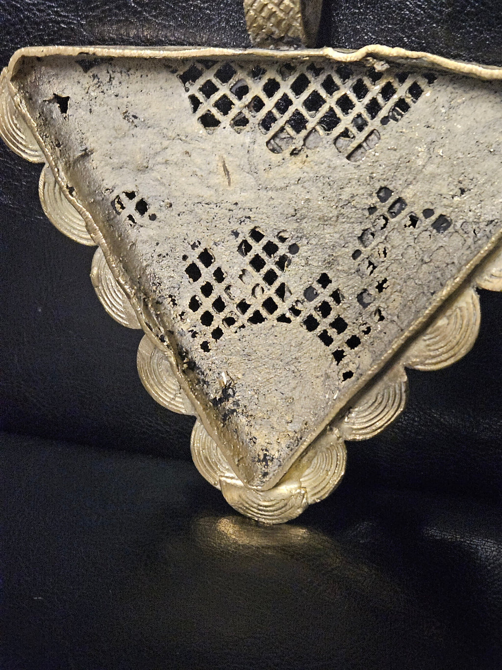 Rear view of the triangular brass pendant showing its open lattice center, spiral borders, and top hanging loop