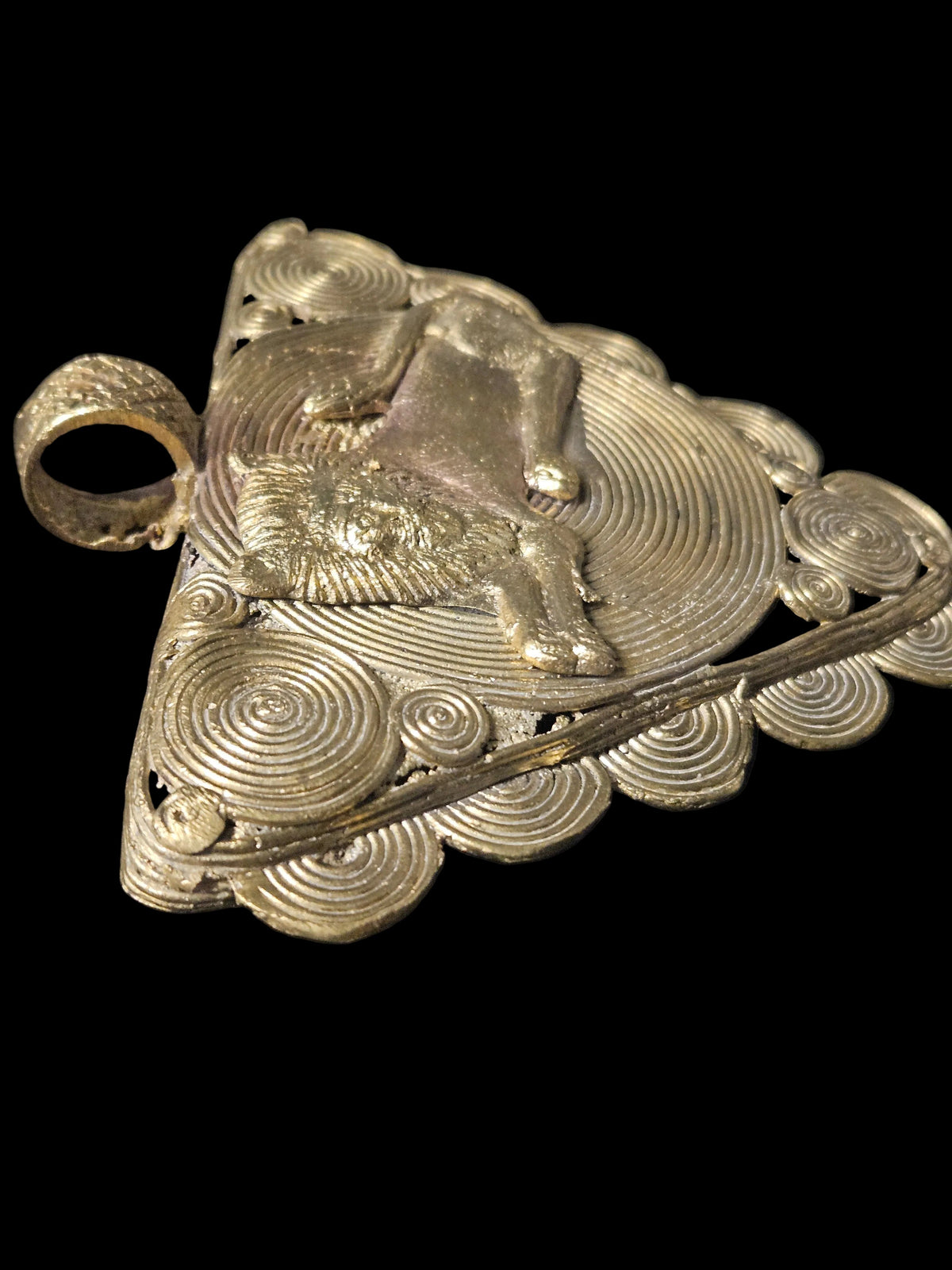 Angled side view of the brass lion pendant showing its thickness, raised lion figure, and hanging loop