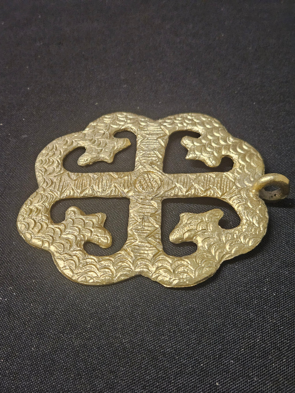 Brass Onyame Dua pendant lying on dark fabric, showing its four open sections, central cross, and hanging loop