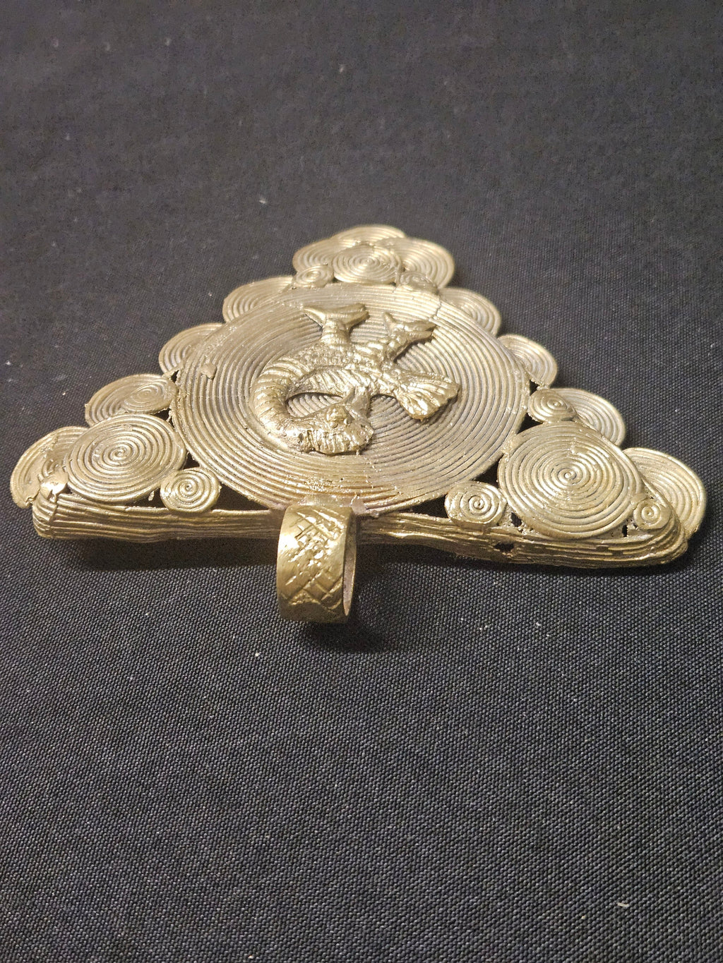 Low side view of the brass Sankofa bird pendant showing its thickness, raised bird detailing, and hanging loop