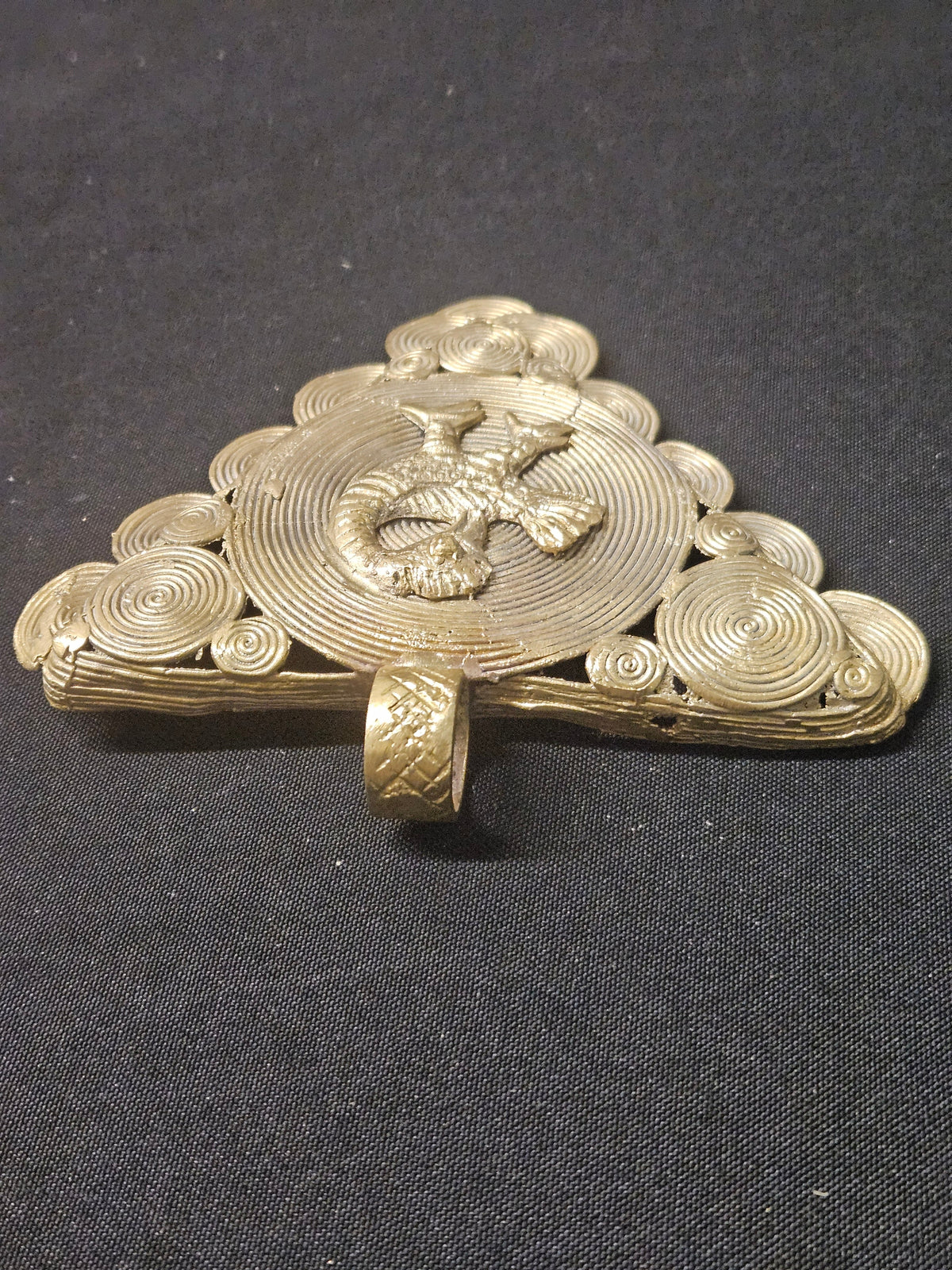 Low side view of the brass Sankofa bird pendant showing its thickness, raised bird detailing, and hanging loop
