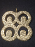 Brass Mati Masie pendant with four circular openwork sections, inward curls, a small diamond-shaped center opening, and a top hanging loop on dark fabric